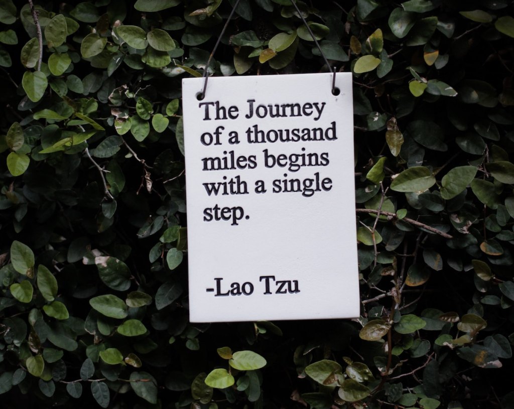 A tile tablet containing a quote from Lao Tzu suspended in front of a wall filled with vines